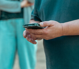 A man in a dark t-shirt stands outside holding a smartphone with both hands while using modern digital technology. © Dmitry