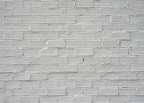 Horizontal rough white painted brick and mortar wall surface with uneven protruding grooved bricks, overfilled joints spilling onto brick faces and chipped flaking mortar  
