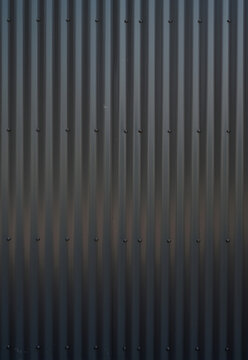 Vertical close up of black corrugated industrial tin siding with uniform vertical ridges, clean undamaged metal surface, light reflection, and minor surface residue marks
