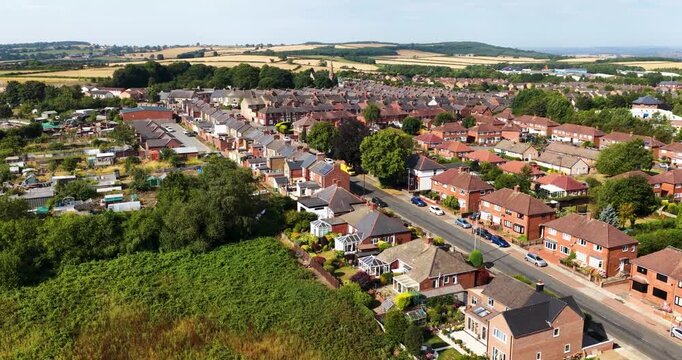 Aerial footage over Shildon in County Durham showing residential streets traditional terraced houses gardens allotments mature trees and surrounding farmland across the northern English countryside