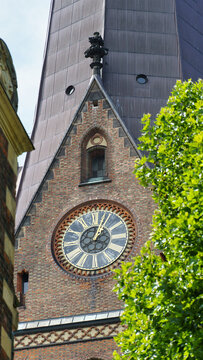 View of the historic brick tower and clock face of the St. Nikolai Memorial, featuring intricate Gothic architecture and surrounding green foliage in Hamburg, Hamburg, Germany.