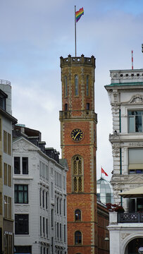 View of the historic Alte Post clock tower with a rainbow flag flying at the top, surrounded by ornate urban architecture in Hamburg, Hamburg, Germany.