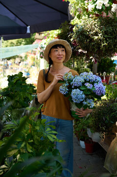 Asian Woman Shopping at Outdoor Flower Market Holding Blue Hydrangea Pot in Summer