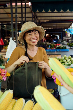 Smiling Asian Woman Market Vendor Selling Fresh Corn at Outdoor Farmers Market Stall