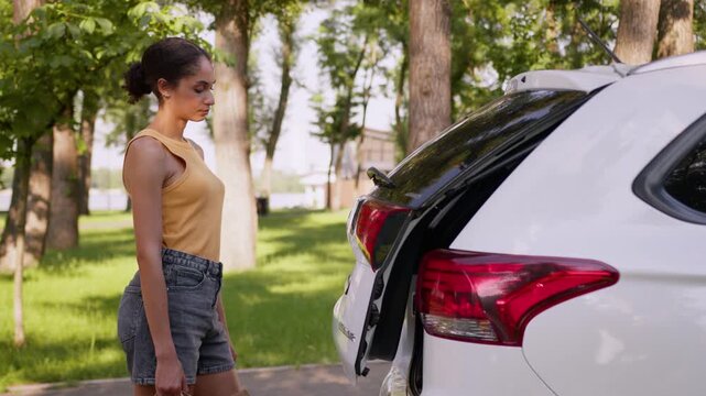 Tired exhausted African American woman loading shopping packages into car trunk city fatigued female shopper delivery customer businesswoman placing bags purchases in automobile outdoor transport auto