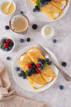 Crepes or thin pancakes with cream cheese, fresh berries and honey on a white plate on a concrete background. Copy space