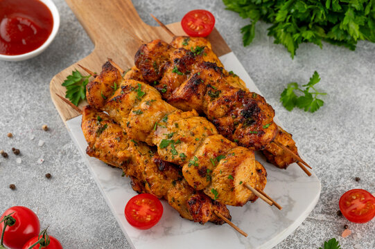 Juicy chicken skewers cooked in an air fryer and served on a wooden board with fresh herbs, cherry tomatoes and dipping sauce. Healthy food. Top view, copy space.