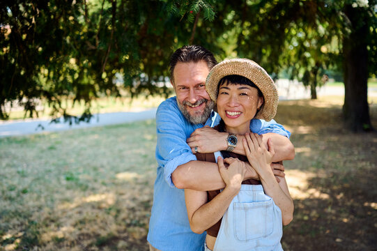 Smiling Couple Hugging in Park &mdash; Asian Woman and Man Embracing on a Sunny Summer Day