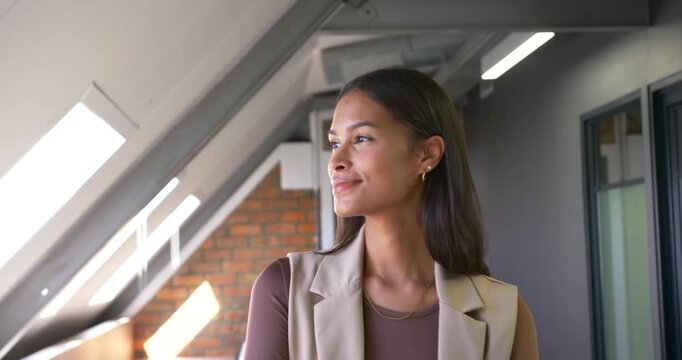 African American woman in blazer standing at skylight in loft, sun drawing head turning, copy space