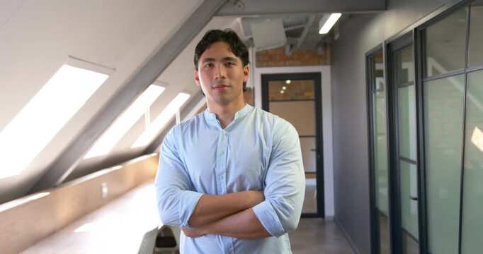 Asian man 20s in blue shirt arms-crossed camera tightening shifting smiling posing under skylights