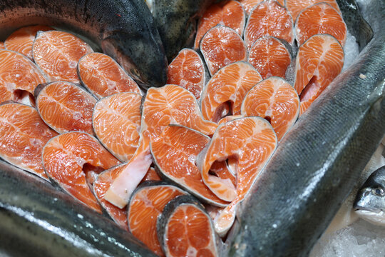 Bright orange salmon fillets are meticulously arranged on a bed of ice, showcasing their vibrant colors and fresh appearance at a bustling seafood market.