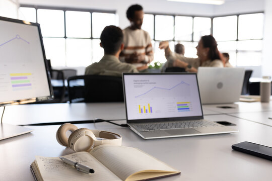 Diverse coworkers presenting and discussing line graph on open laptop in modern meeting area