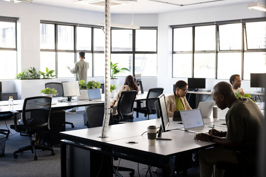 Diverse coworkers working in open office, man writing at right with laptop and notebook, copy space