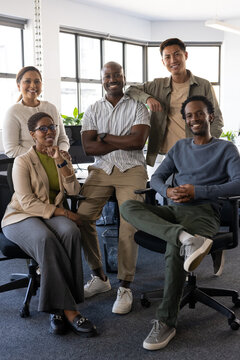 Diverse coworkers in business clothes smiling sitting on chairs in office by windows with backpack