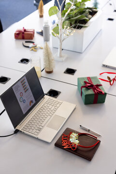 Silver laptop is displaying colorful charts on white modular table at office with gifts