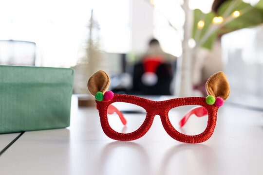 Novelty red holiday glasses are resting on tabletop near green gift and lit plant at office