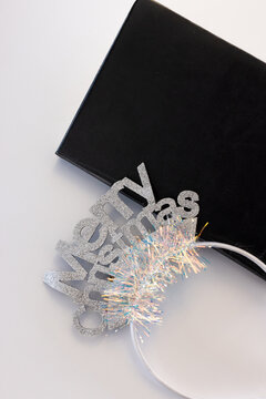Silver glitter headband is resting partly over black notebook on white table, tinsel, copy space