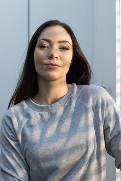 Female posing in front of paneled wall wearing grey crewneck sweatshirt and stud earrings