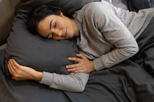 Female lying on bed wearing light gray long-sleeve top, resting head on dark gray pillow