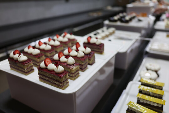 In a lively bakery, colorful layers of cakes showcase whipped cream and fresh strawberries on top. Pastry chefs hustle to prepare the day's orders, filling the air with sweet aromas.