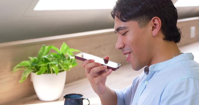 Asian man mid-20s holding phone near mouth, replying to voice note desk under skylight, copy space