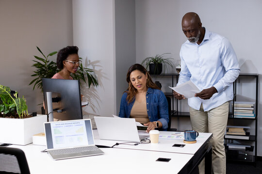 African American team meeting at white table, seated woman working on laptop and holding reports