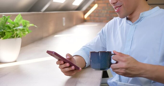 Camera pulling back, showing man holding pink phone and blue mug, reacting to message at counter