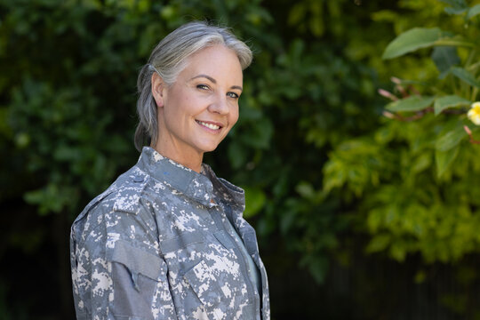 Woman soldier standing in garden wearing gray camo jacket with pockets and epaulets