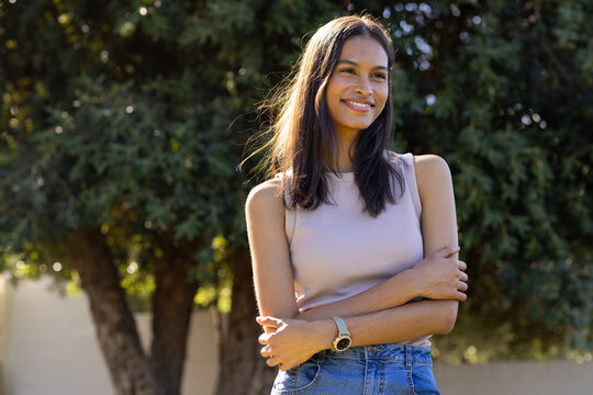 African American woman standing in sleeveless top and jeans by garden wall sunlight catching watch