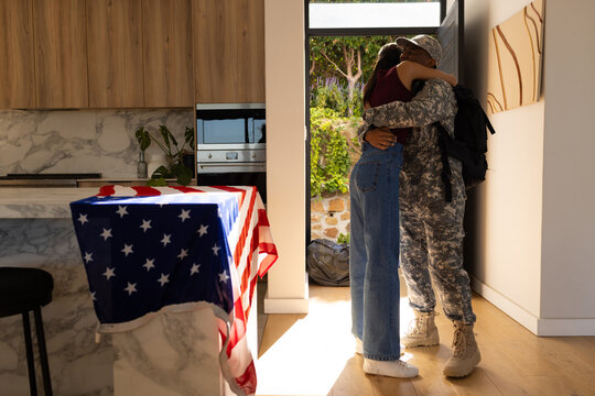 African American couple hugging at doorway, soldier in camo tan combat boots, US flag, copy space
