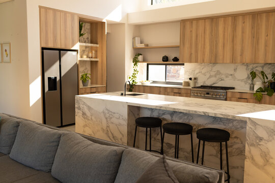 Marble waterfall island sitting in open-plan kitchen, showing sink, matte faucet and three stools
