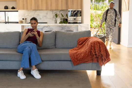 African American couple in living room, woman checking phone, man entering in uniform carrying bag