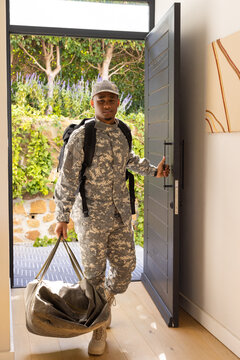 African American male soldier carrying olive duffel wearing black backpack stepping through foyer