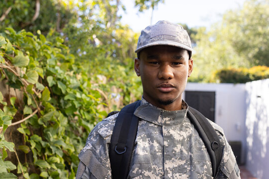 African American man standing on paved pathway in garden, wearing digital camouflage and backpack