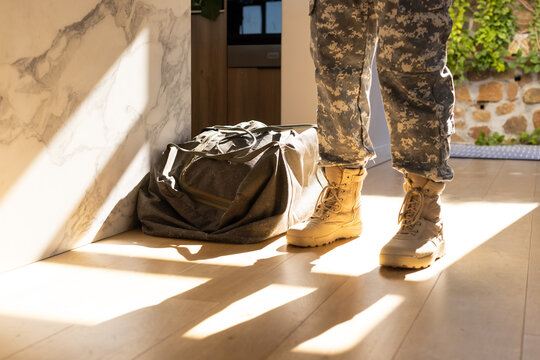 Man wearing camouflage trousers and tan tactical boots standing in foyer by duffel, copy space