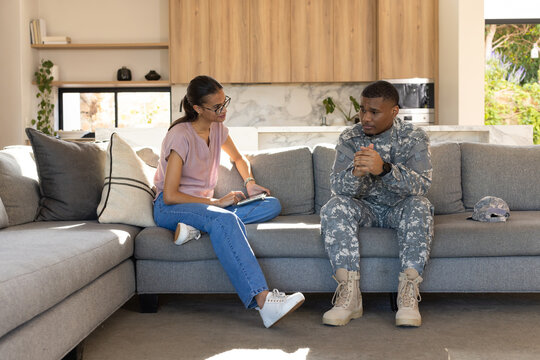 African American woman taking notes on notebook while soldier in camo sitting on sofa with helmet