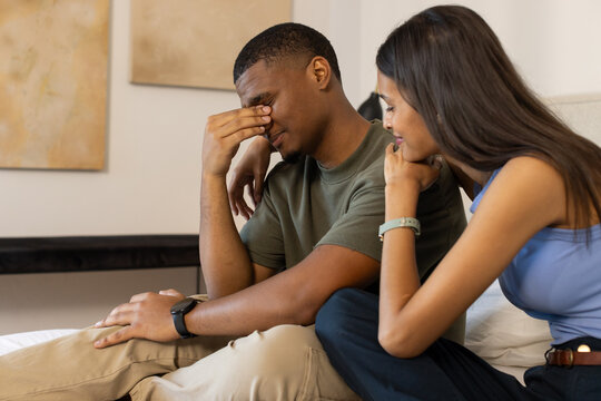 African American couple sitting on bed at home, woman comforting distressed man wearing watch