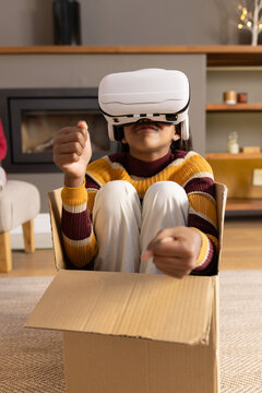 African American teen sitting in cardboard box in living room wearing VR headset, striped sweater