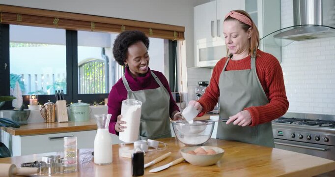 Diverse female friends aproned starting recipe, pouring flour into metal sifter at kitchen island