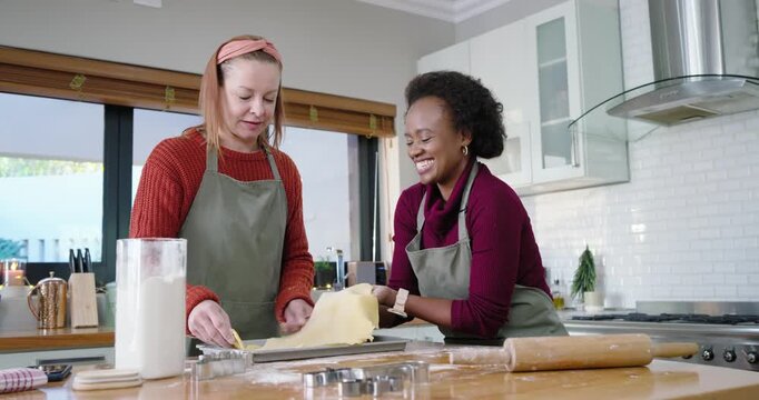 African American friends unrolling dough, lifting and cutting in kitchen with cutters for cookies