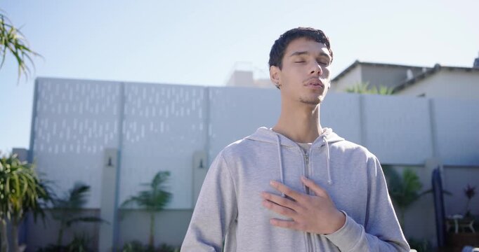 African American man wearing hoodie standing on patio, breathing for calm as camera pulling back
