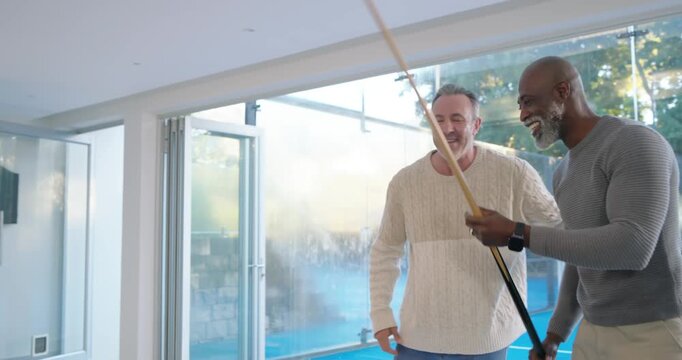 Diverse male friends laughing after initial shot, one lining up shot on black pool table