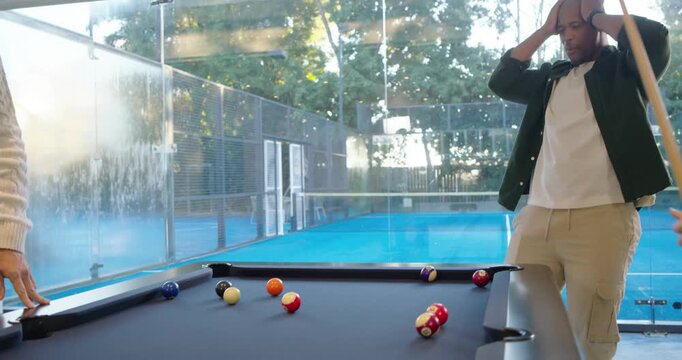 Four men playing pool in game room, reacting to near-miss cue, guiding mature man taking shot