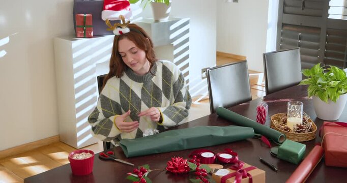 Woman in argyle sweater antlers placing green paper cutting folding gift at table for holidays