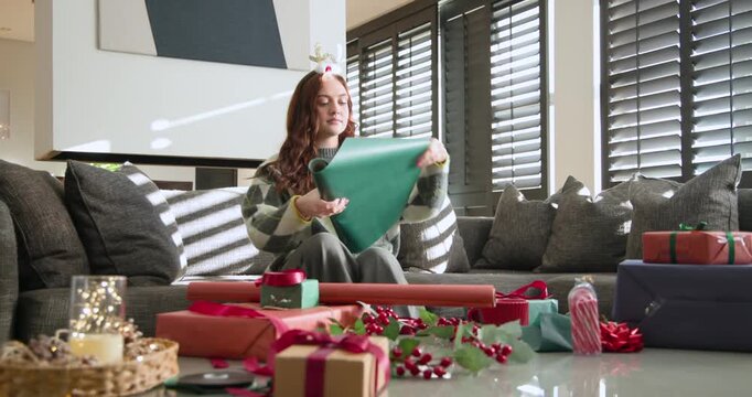Woman entering carrying red mug, green roll sitting on sofa and wrapping gifts using scissors