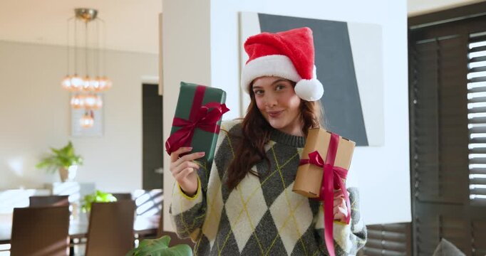 Adult woman in argyle sweater holding gifts, filming at home, placing green box on Santa hat