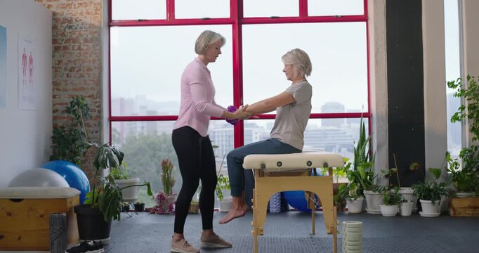 Female therapist and client doing arm raises for rehab, therapist handing weights at studio table