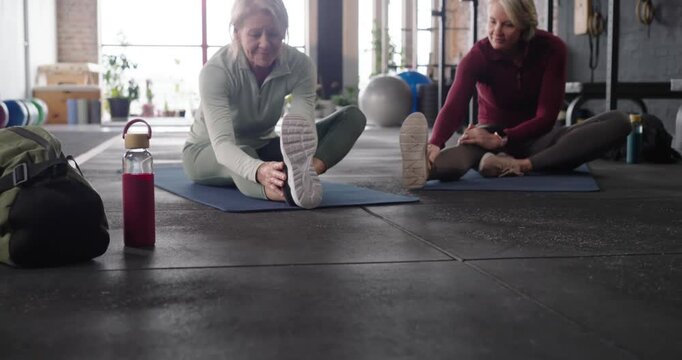 Female partners placing bottle stretching hamstrings on blue mats warming up in studio in gym gear