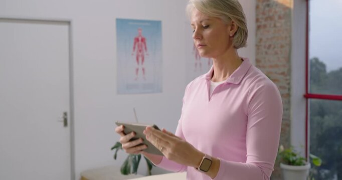 Middle-aged female therapist reviewing notes on tablet while camera slowly zooming out in clinic