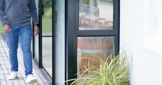 Male entering sliding glass door, walking on wooden deck, leaning against window posing for camera